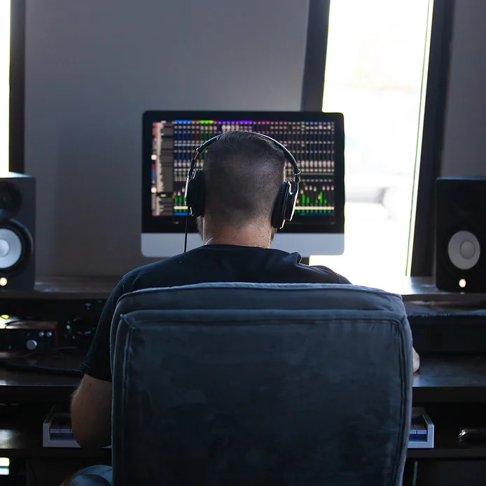 Josiah Smiley mixing at his studio desk, wearing headphones in front of a DAW session